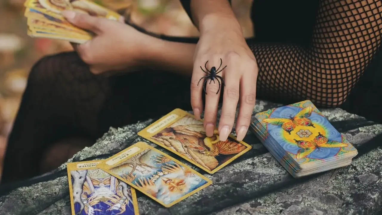 Ręka z pierścieniem w kształcie pająka rozkłada karty tarota. Czy to horoskop miesięczny lew tarot?