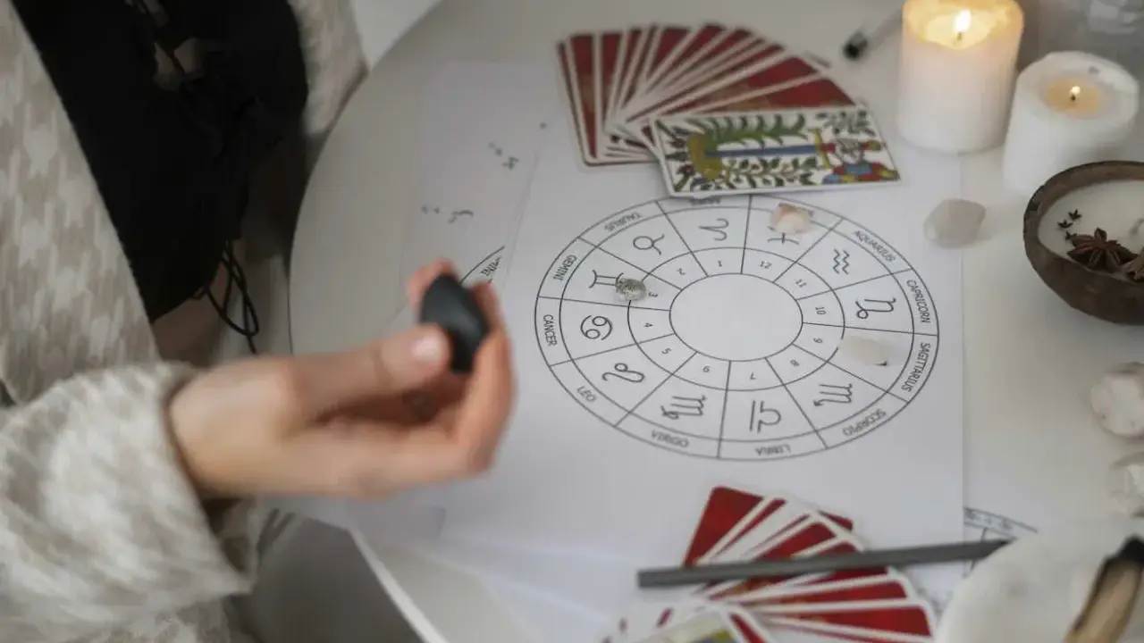 Astrologiczna mapa nieba z symbolami zodiaku, talie kart i świece. Wenus w Strzelcu zapowiada podróże i nowe znajomości.