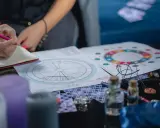 Osoba pisze w notatniku, obok wykresy astrologiczne, świece i talizmany. Analiza 12 dom astrologia.