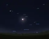 Jasny Jowisz w Byku świeci na nocnym niebie, otoczony gwiazdami i mgławicami. Obok widoczny Księżyc i Saturn.