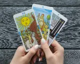 Ręce trzymają karty tarota: Słońce, Dziewiątka Monet i Czwórka Mieczy. To może być tarot miesięczny dla Raka.