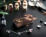Stawianie tarota samemu sobie: talia kart w steampunkowym stylu, wahadełko i runy na czarnym tle.