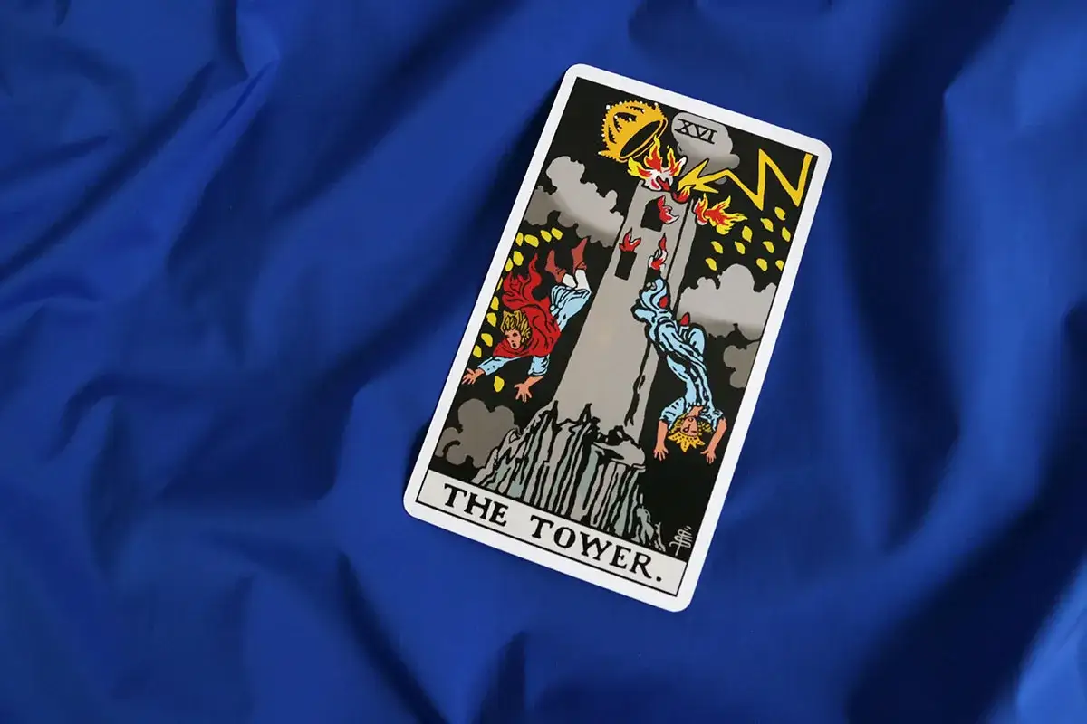 Karta the tower tarot przedstawia wieżę płonącą od uderzenia pioruna, z której spadają ludzie.