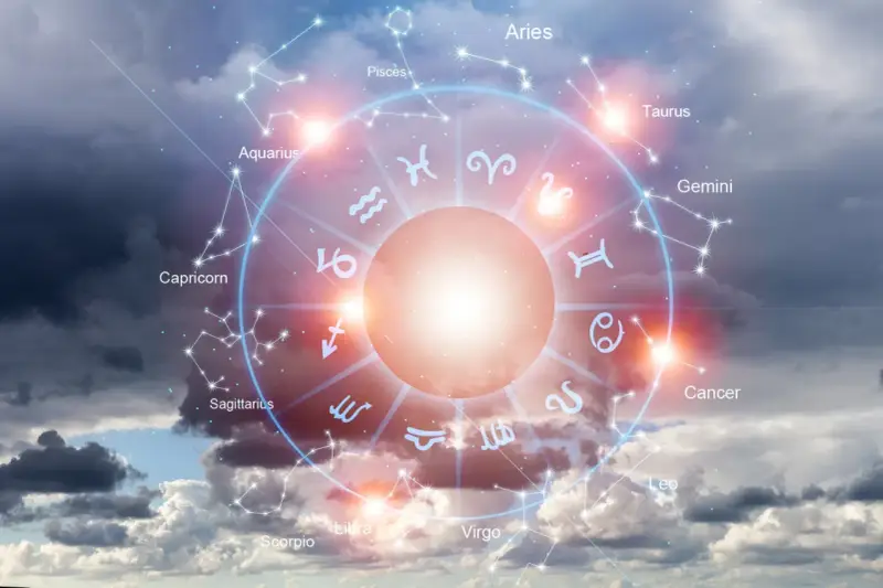 Koło zodiaku na tle burzowych chmur. Słońce w Baranie rozświetla centrum, a wokół widnieją gwiazdozbiory i symbole znaków.